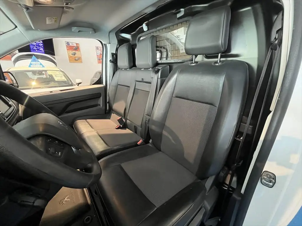 Intérieur du Peugeot Expert Fourgon 2019, vue côté conducteur montrant les sièges noirs et la cloison métallique blanche.