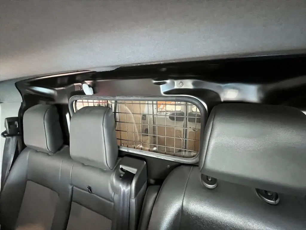 Vue intérieure arrière du Peugeot Expert Fourgon blanc de 2019, montrant les sièges noirs et la grille de séparation du coffre.