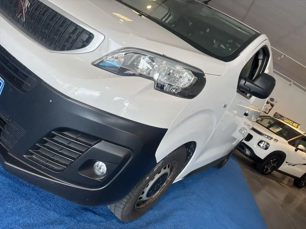 Vue 3/4 avant droit d'un Peugeot Expert Fourgon blanc avec pare-chocs noir et rétroviseur noir en showroom.