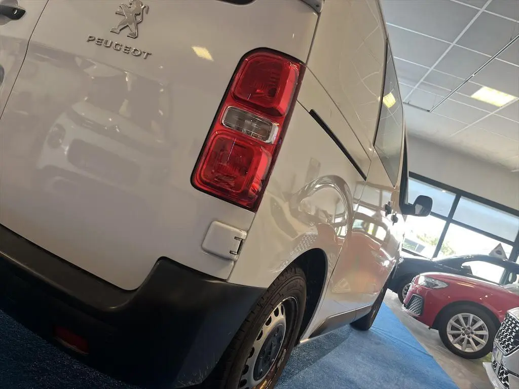 Vue 3/4 arrière droite d'un Peugeot Expert Fourgon blanc dans un showroom avec feux arrière rouges visibles.