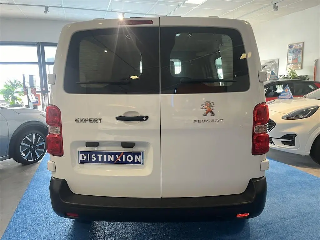 Vue arrière d'un Peugeot Expert Fourgon blanc exposé en showroom avec vitres teintées et logo visible.