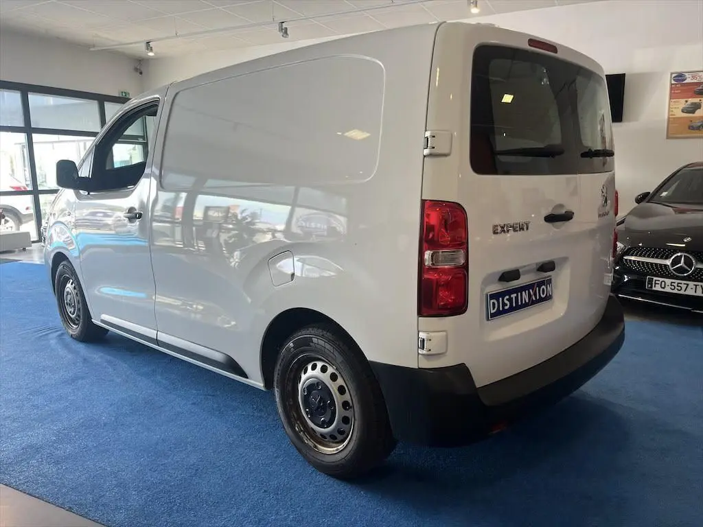 Vue 3/4 arrière droite d'un Peugeot Expert Fourgon blanc exposé en showroom avec plaque Distinxion.