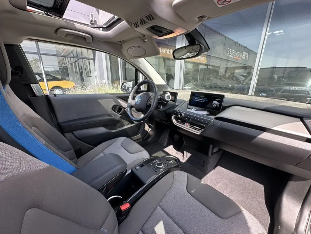 Intérieur avant de la BMW i3 bleue 2022, vue côté conducteur, avec toit ouvrant et tableau de bord moderne.
