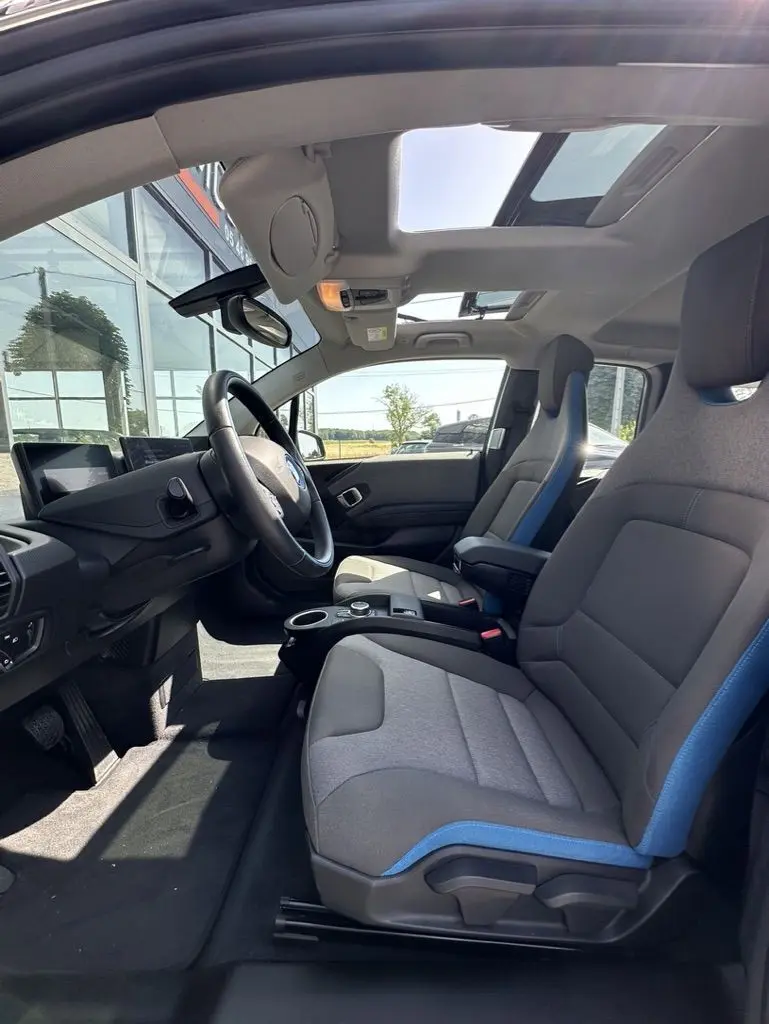 Vue intérieure côté conducteur de la BMW i3 2022 avec sièges gris et bleu et toit ouvrant panoramique.