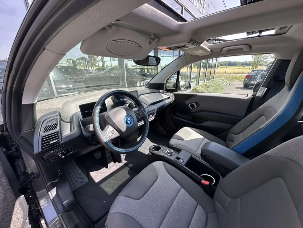 Intérieur de la BMW i3 2022 vu côté conducteur, avec volant bleu et sièges gris clair en tissu.