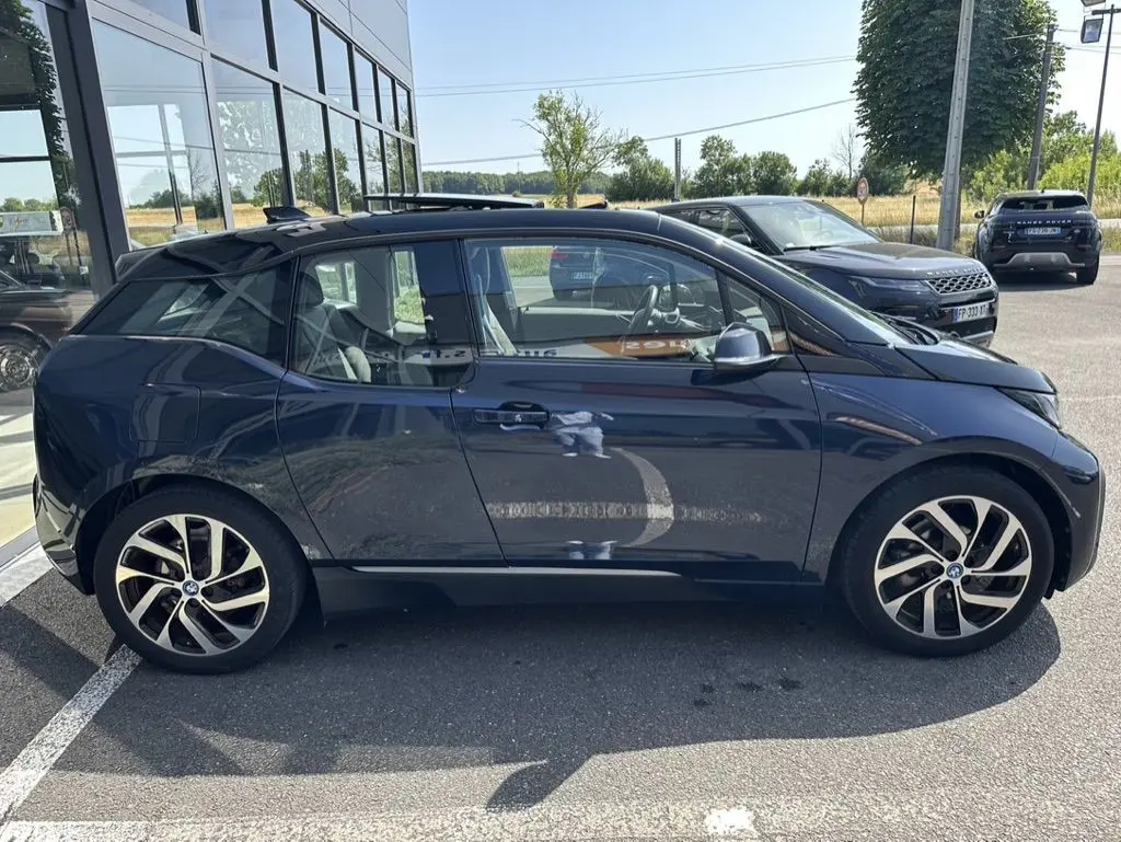 Profil côté gauche d'une BMW i3 électrique bleue 2022, avec ses jantes distinctives en alliage et toit noir.