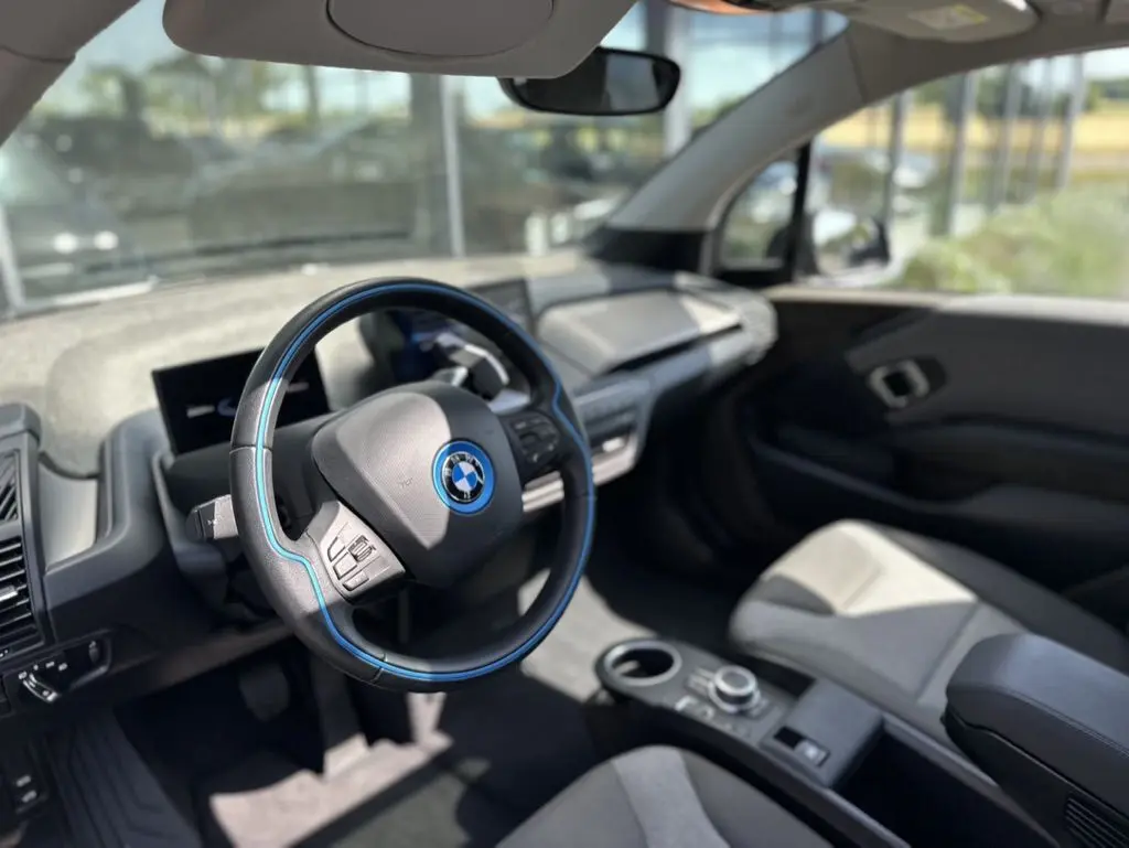 Intérieur de la BMW i3 2022 bleu, vue côté conducteur sur le volant avec surpiqûres bleues et tableau de bord moderne.