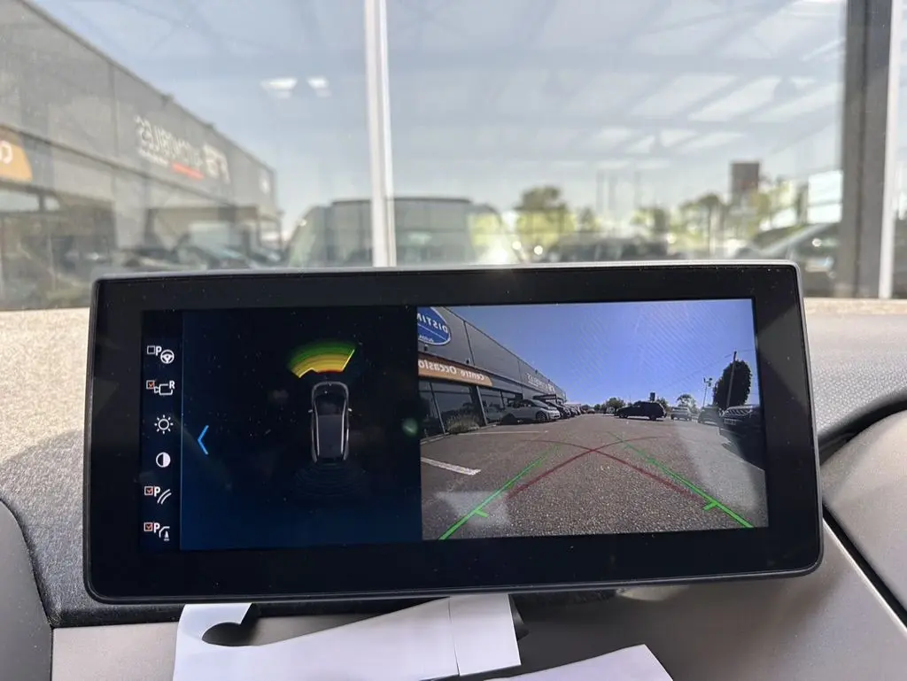 Écran de caméra de recul et capteurs de stationnement dans une BMW i3 bleue, vue intérieure du tableau de bord.