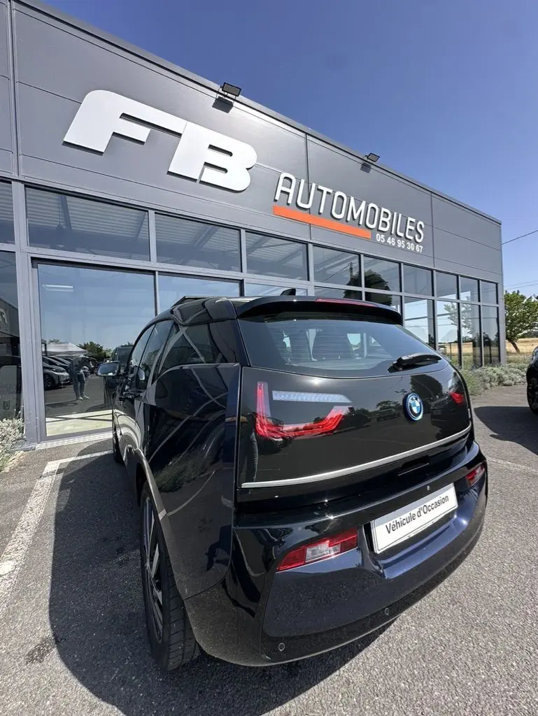 Vue 3/4 arrière d'une BMW i3 noire stationnée devant une concession FB Automobiles par temps clair.