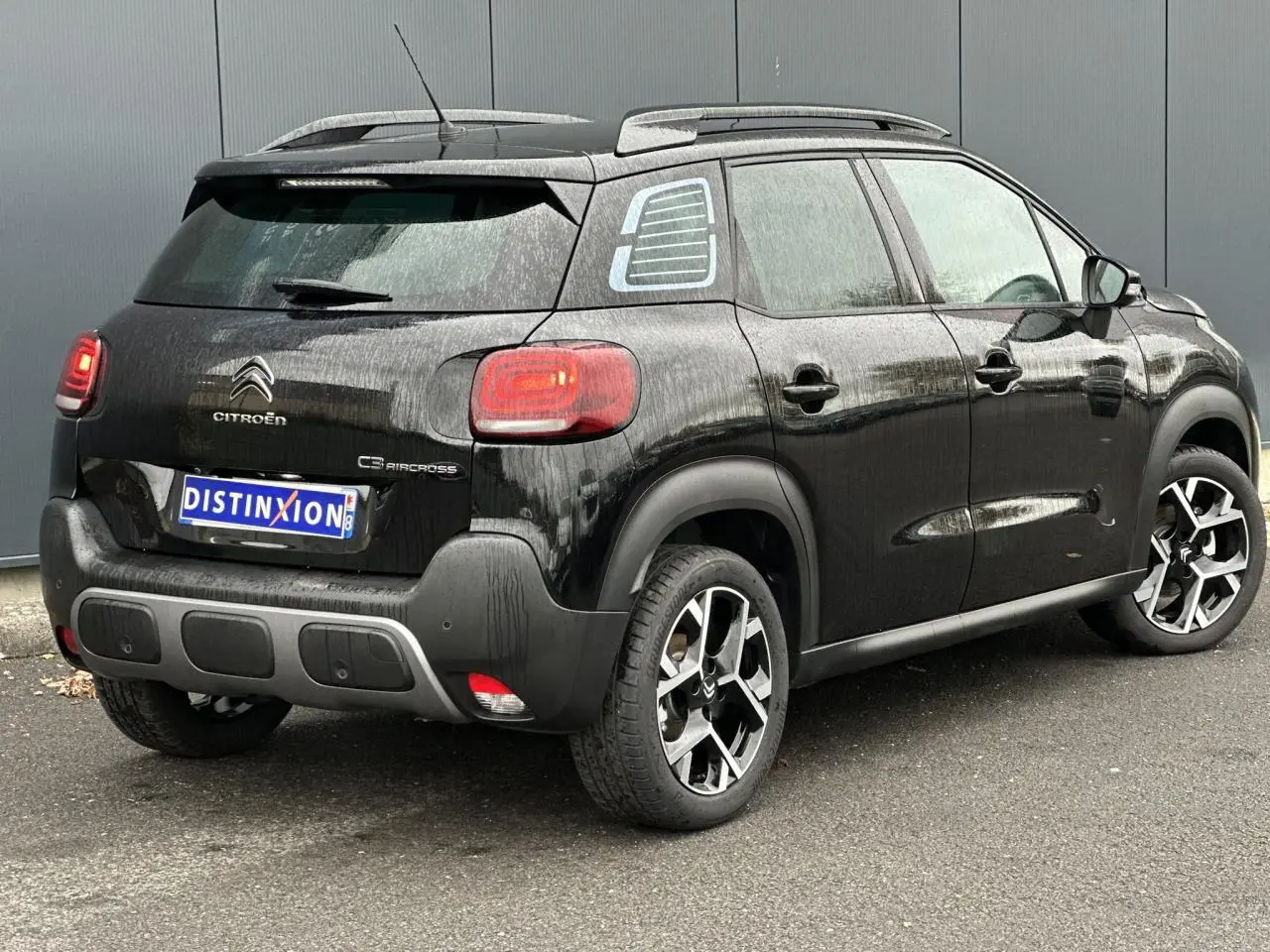 Vue 3/4 arrière droit d'une Citroën C3 Aircross 2024 noir Perla avec jantes alliage et barres de toit.