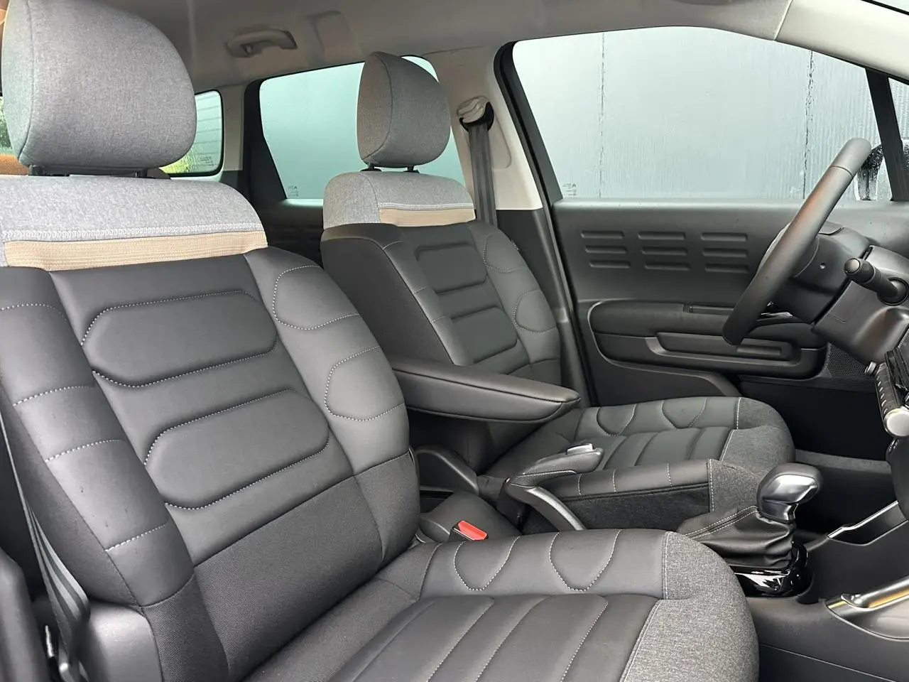 Intérieur de Citroën C3 Aircross 2024, vue côté droit sur sièges mixtes cuir et tissu gris avec accoudoir central.