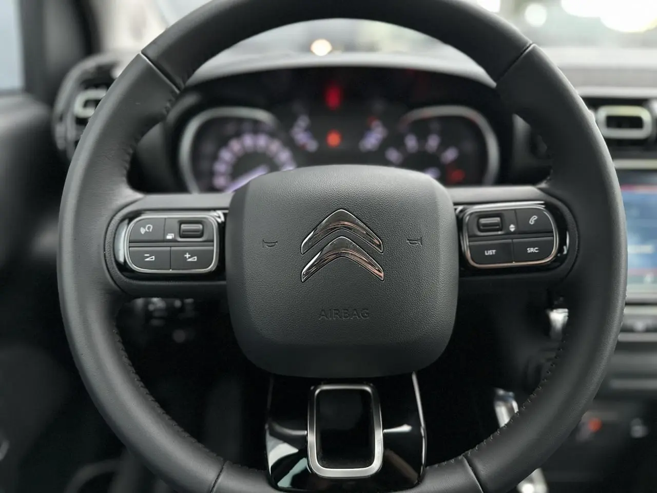 Volant en croûte de cuir noir de Citroën C3 Aircross 2024 avec commandes audio intégrées et tableau de bord flou.