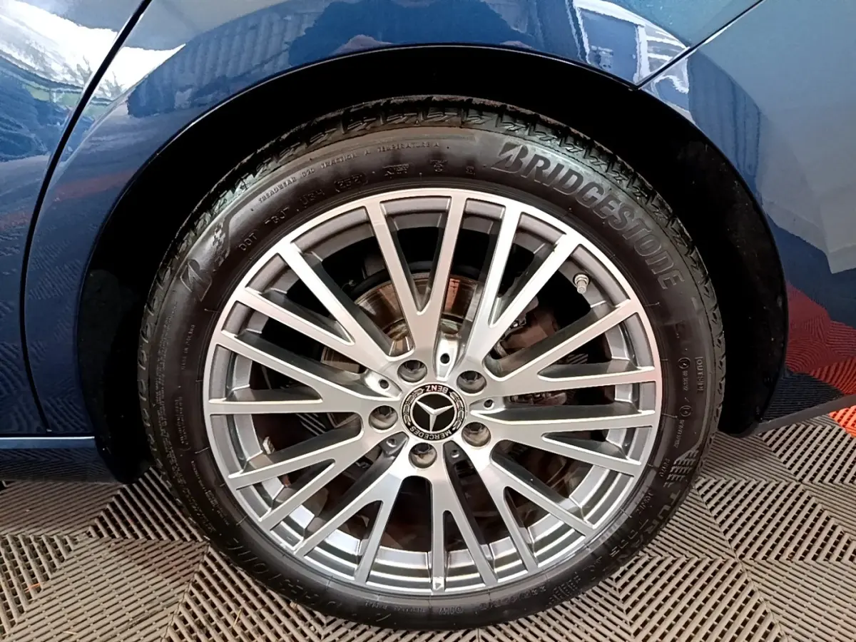 Gros plan sur la jante alu multi-branches argentée et pneu Bridgestone d'une Mercedes CLA 180 d Business Line bleu foncé, côté arrière.