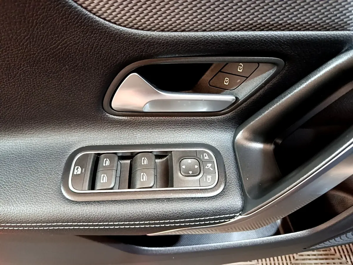Gros plan sur la porte côté gauche d’une Mercedes CLA 180 d blanche, montrant la poignée alu et les commandes des vitres.