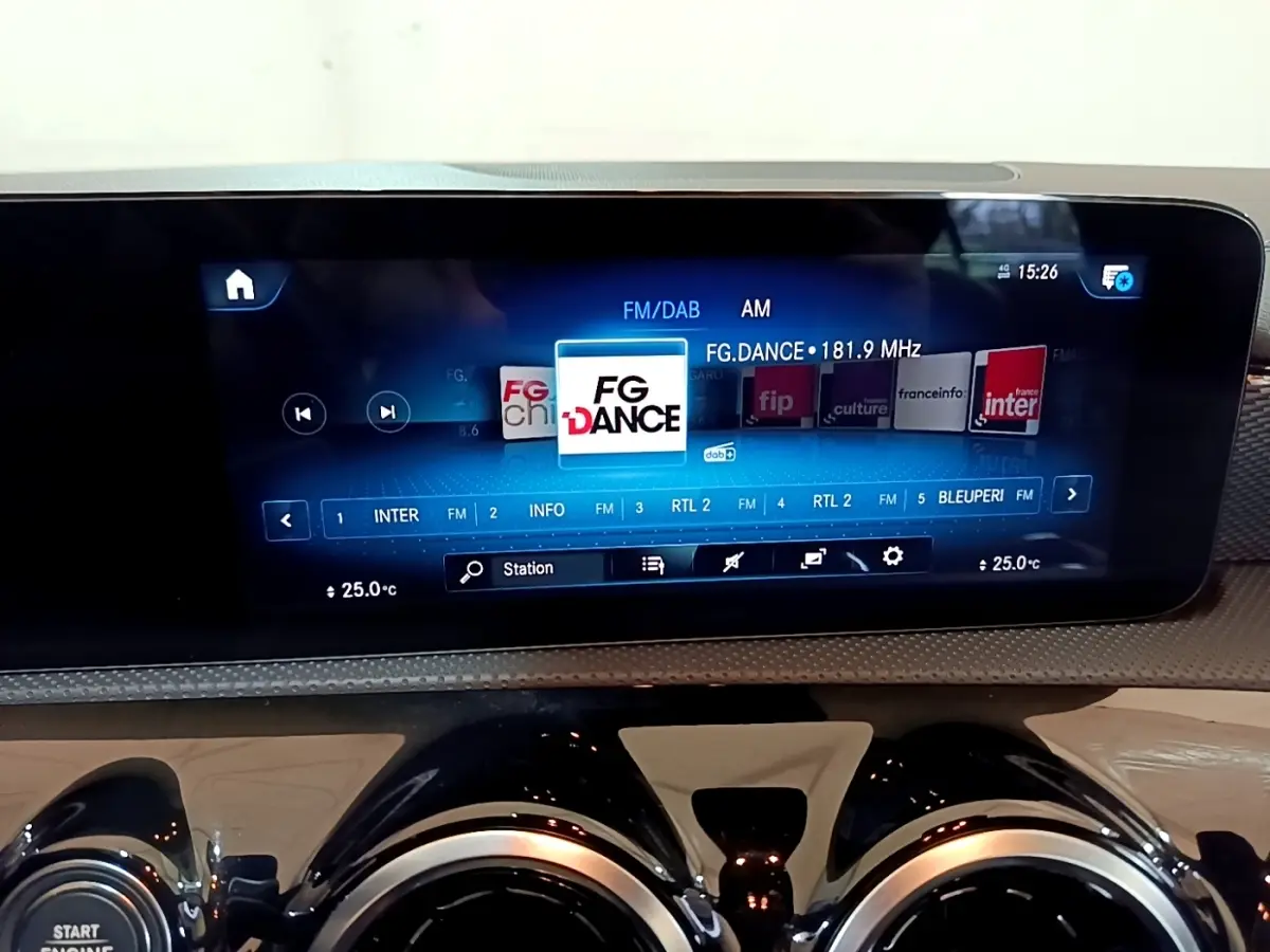 Vue rapprochée de l’écran tactile multimédia et des aérateurs ronds noirs du tableau de bord d’une Mercedes CLA blanche.