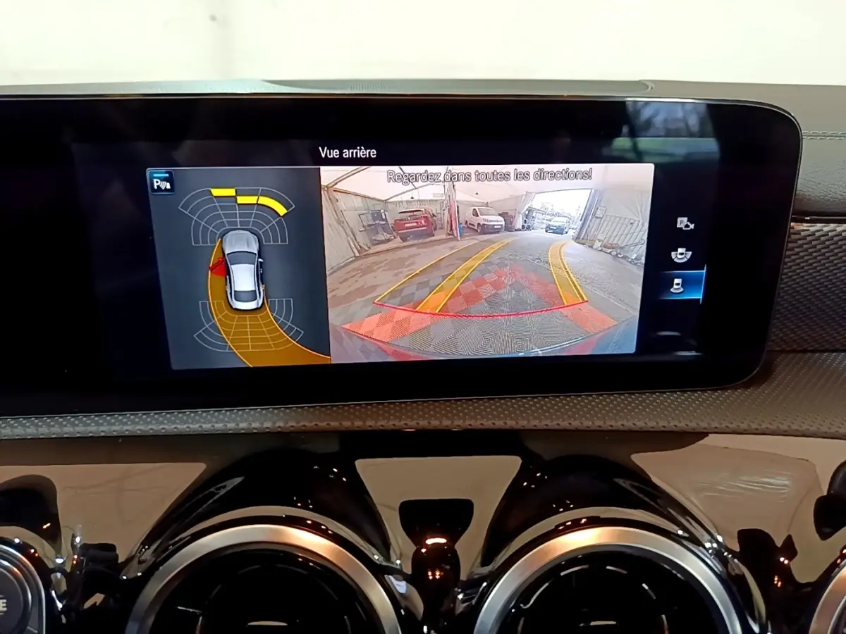 Écran tactile intérieur montrant la caméra de recul et l’aide au stationnement du Mercedes CLA 180 d blanc.