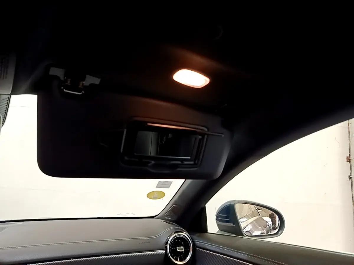 Détail de l'intérieur côté passager d'une Mercedes CLA 180 d Business Line blanche, avec pare-soleil et miroir éclairé.