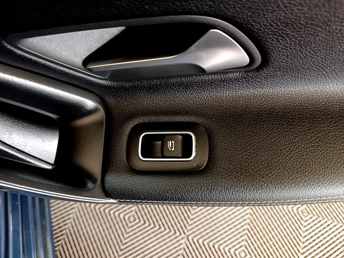 Gros plan sur le bouton de commande de la fermeture électrique de la vitre, sur la porte intérieure noire d’une Mercedes CLA 180 d blanche.