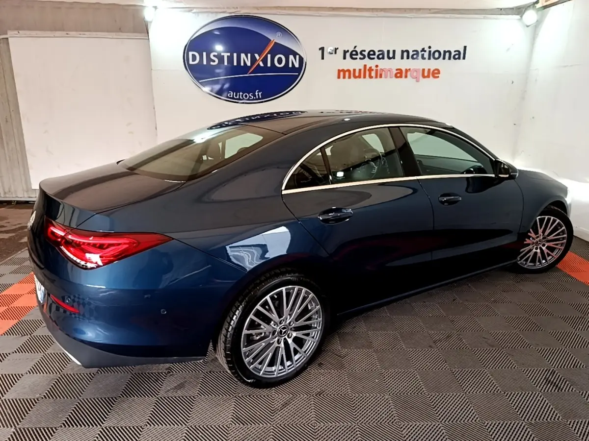Vue 3/4 arrière droite d'une Mercedes CLA 180 d Business Line bleu foncé avec jantes alliage et feux arrière LED allumés.
