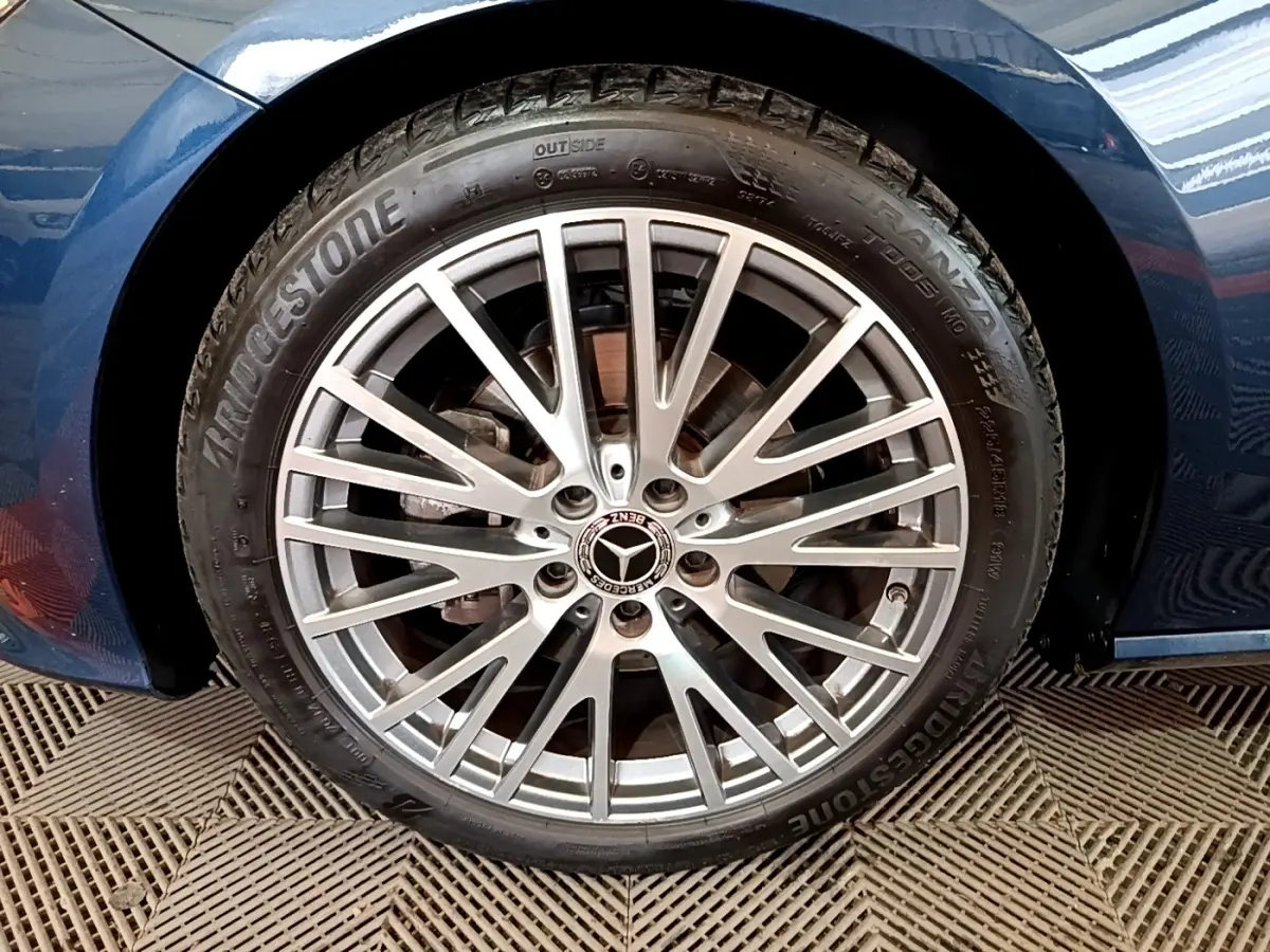 Gros plan sur la jante alliage argentée avec logo Mercedes, montée sur un pneu Bridgestone, carrosserie bleu foncé visible.