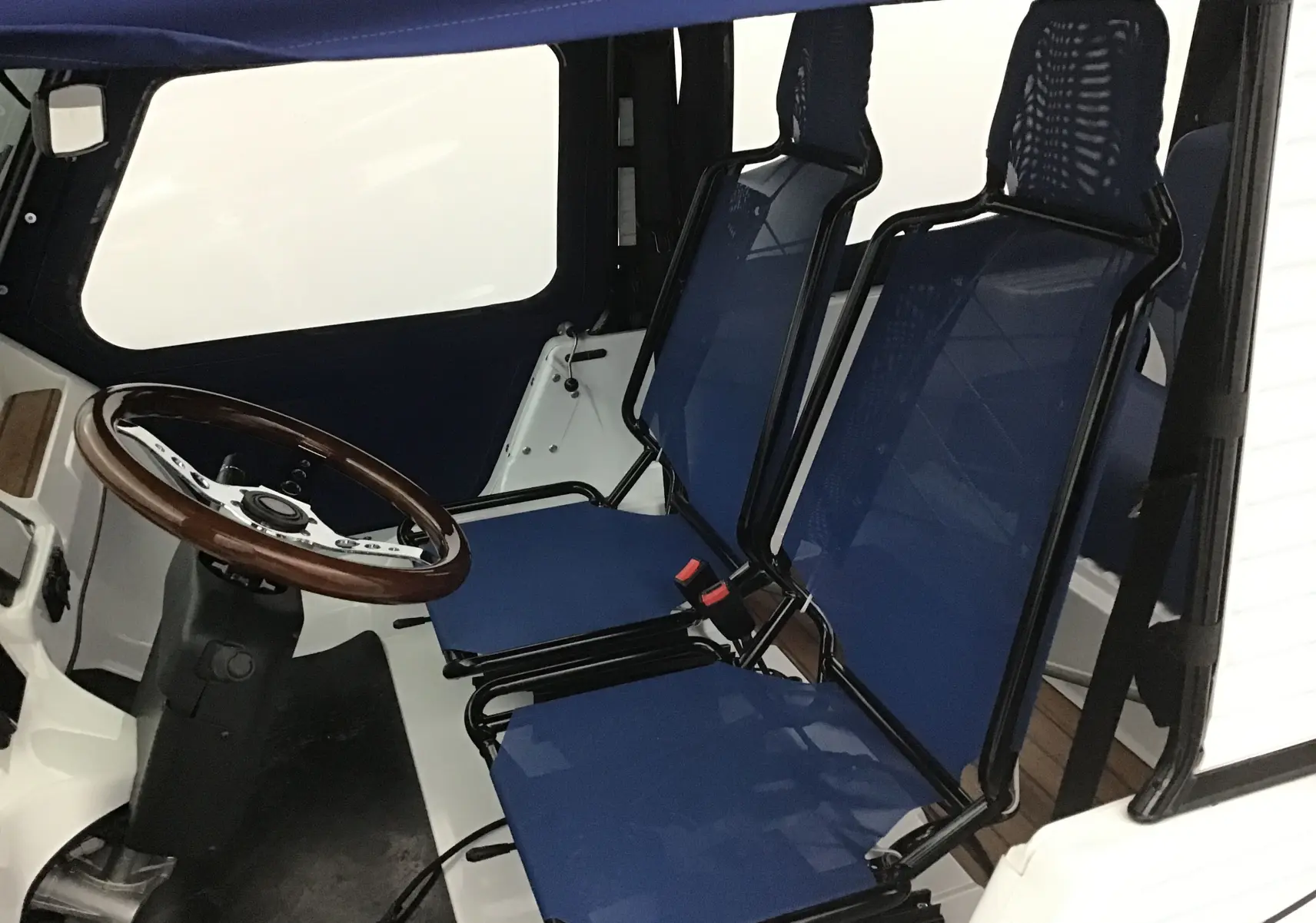 Vue intérieure avant du MLT E-STORY ICONE 2024 blanc/bleu avec sièges et volant bois, plancher teck et fermeture Sunbrella bleue.