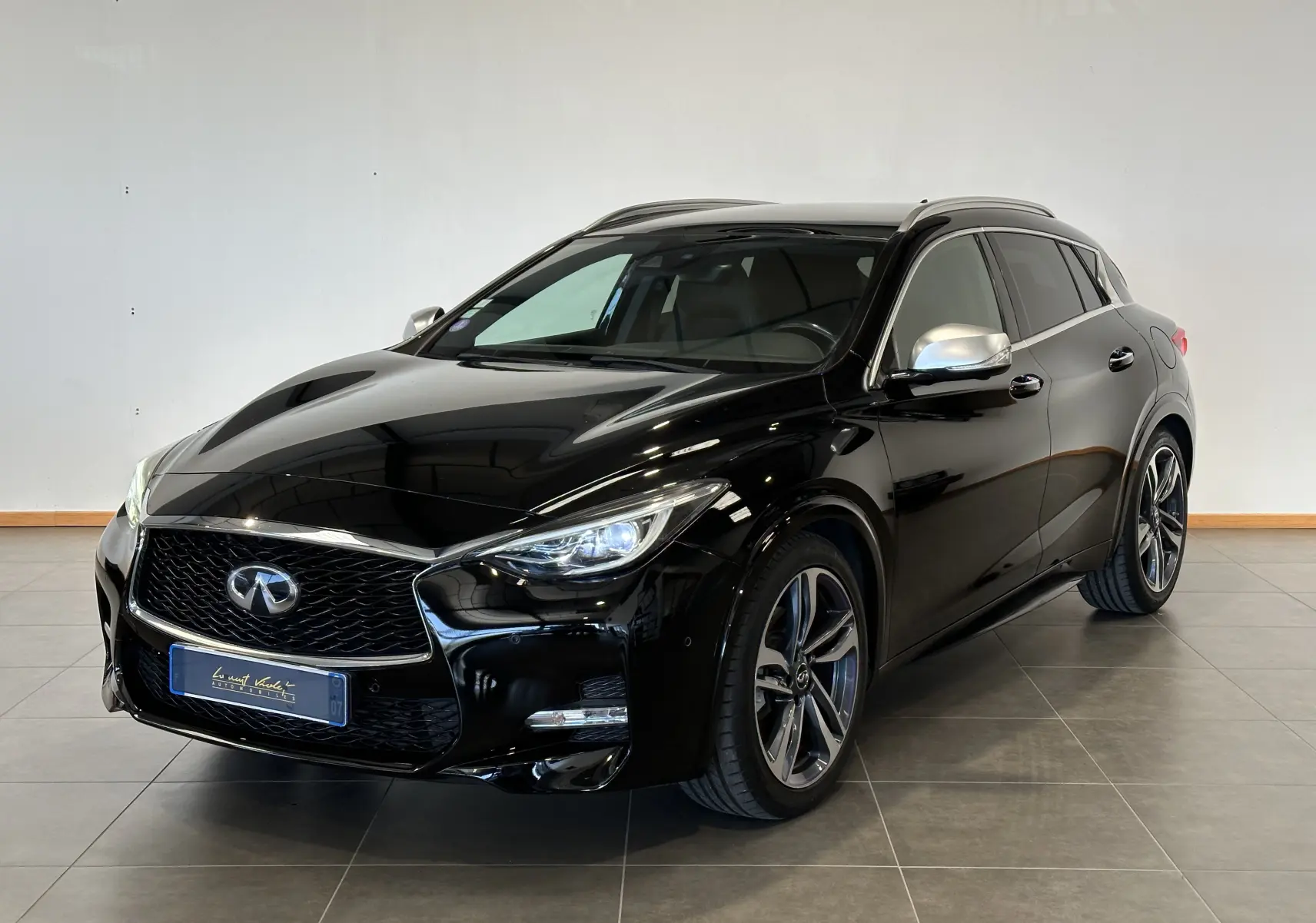Vue 3/4 avant droite d'une Infiniti Q30 noire 2016 avec jantes alliage et rétroviseurs argentés en intérieur showroom.