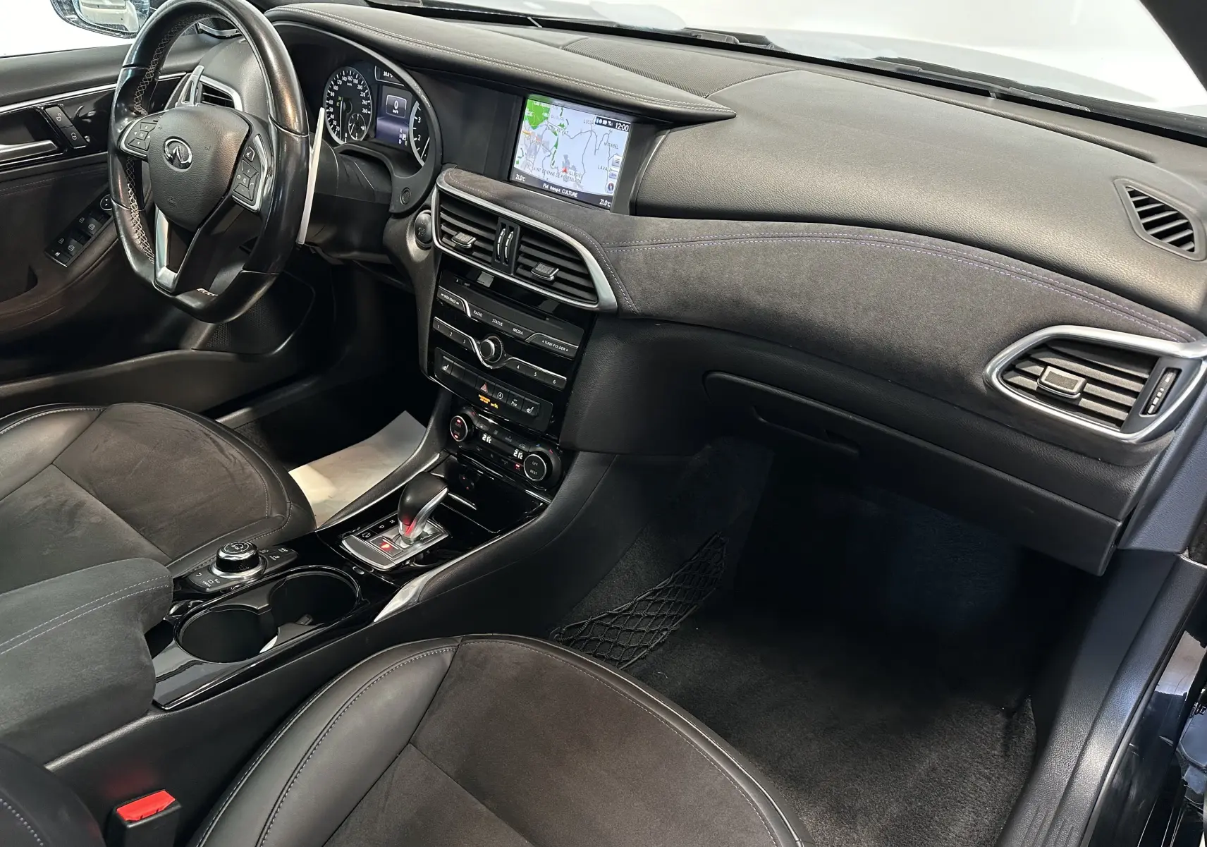 Vue intérieure côté conducteur de l'INFINITI Q30 noire, mettant en valeur le tableau de bord avec écran GPS et volant multifonction.