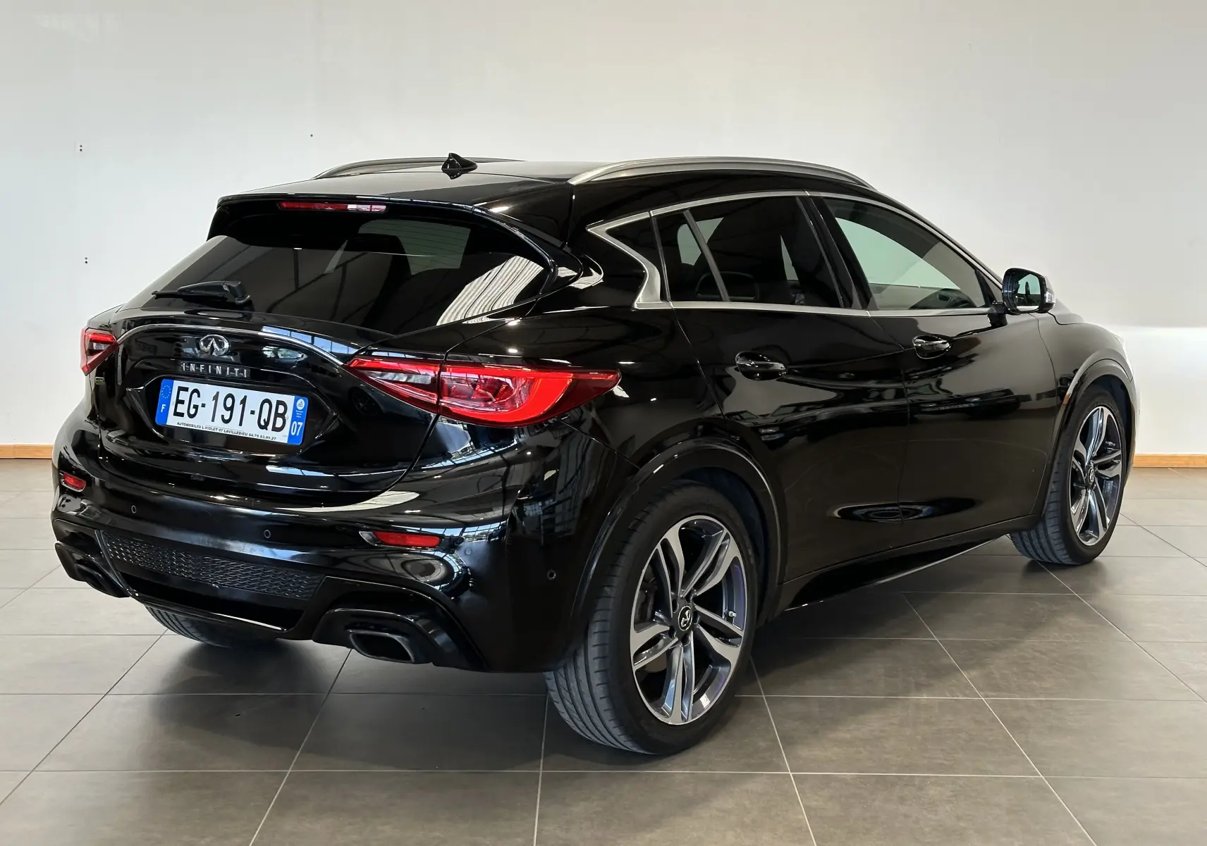 Vue 3/4 arrière droite d'une Infiniti Q30 noire 2016 avec jantes alliage et vitres teintées en intérieur showroom.