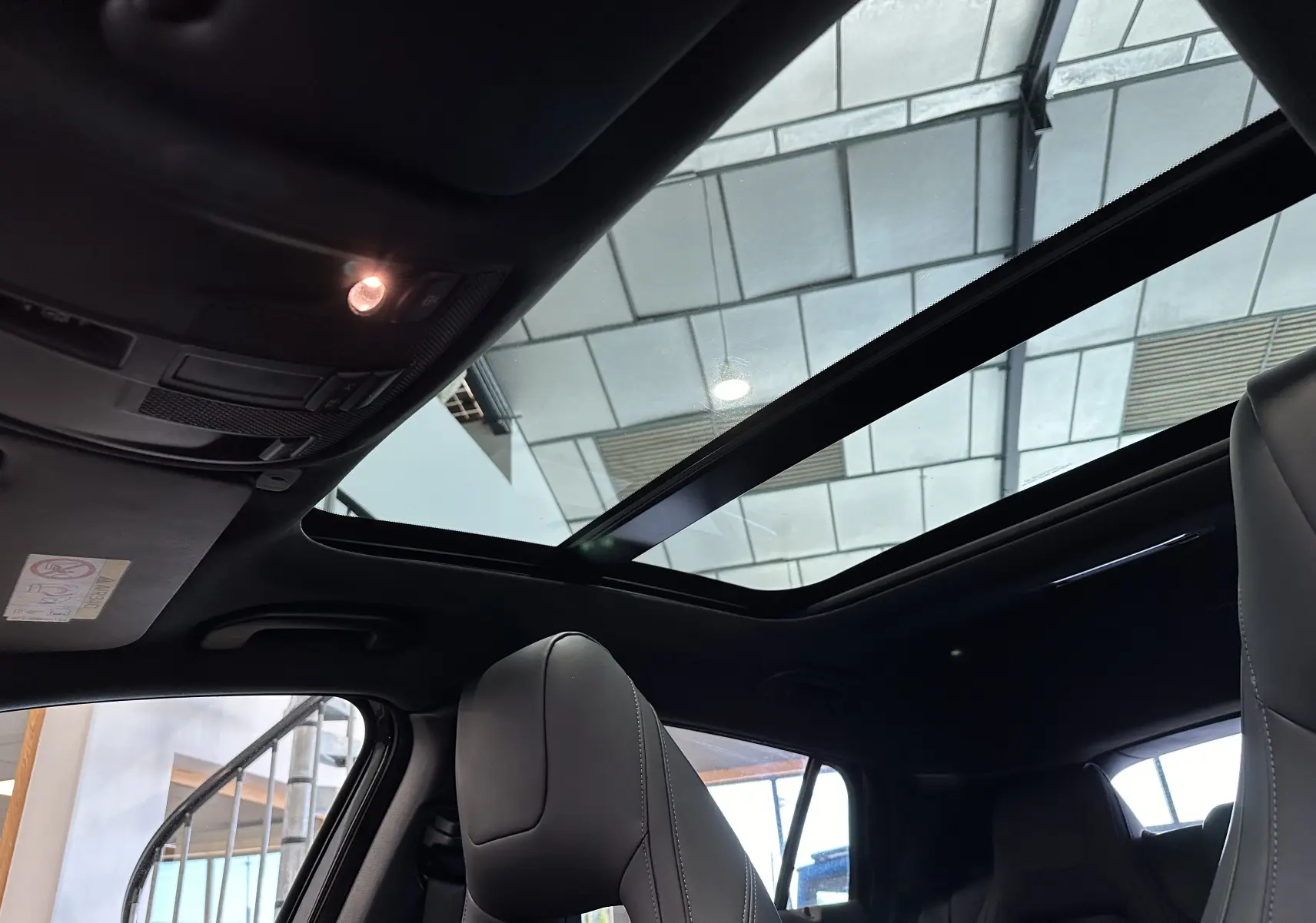 Toit panoramique ouvert vu de l'intérieur sur une INFINITI Q30 noire, avec sièges avant en cuir et ambiance sombre.