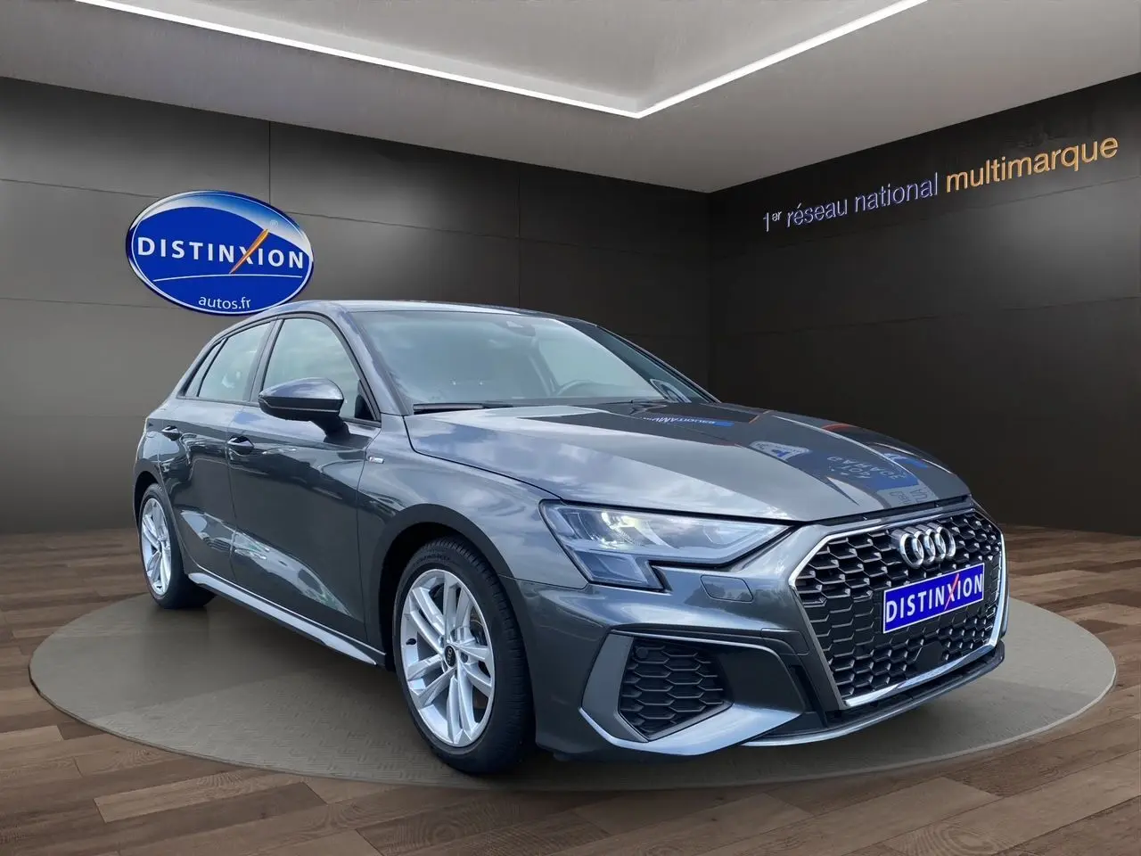 Audi A3 Sportback gris Daytona vue 3/4 avant droit, avec calandre hexagonale et jantes alliage argentées.