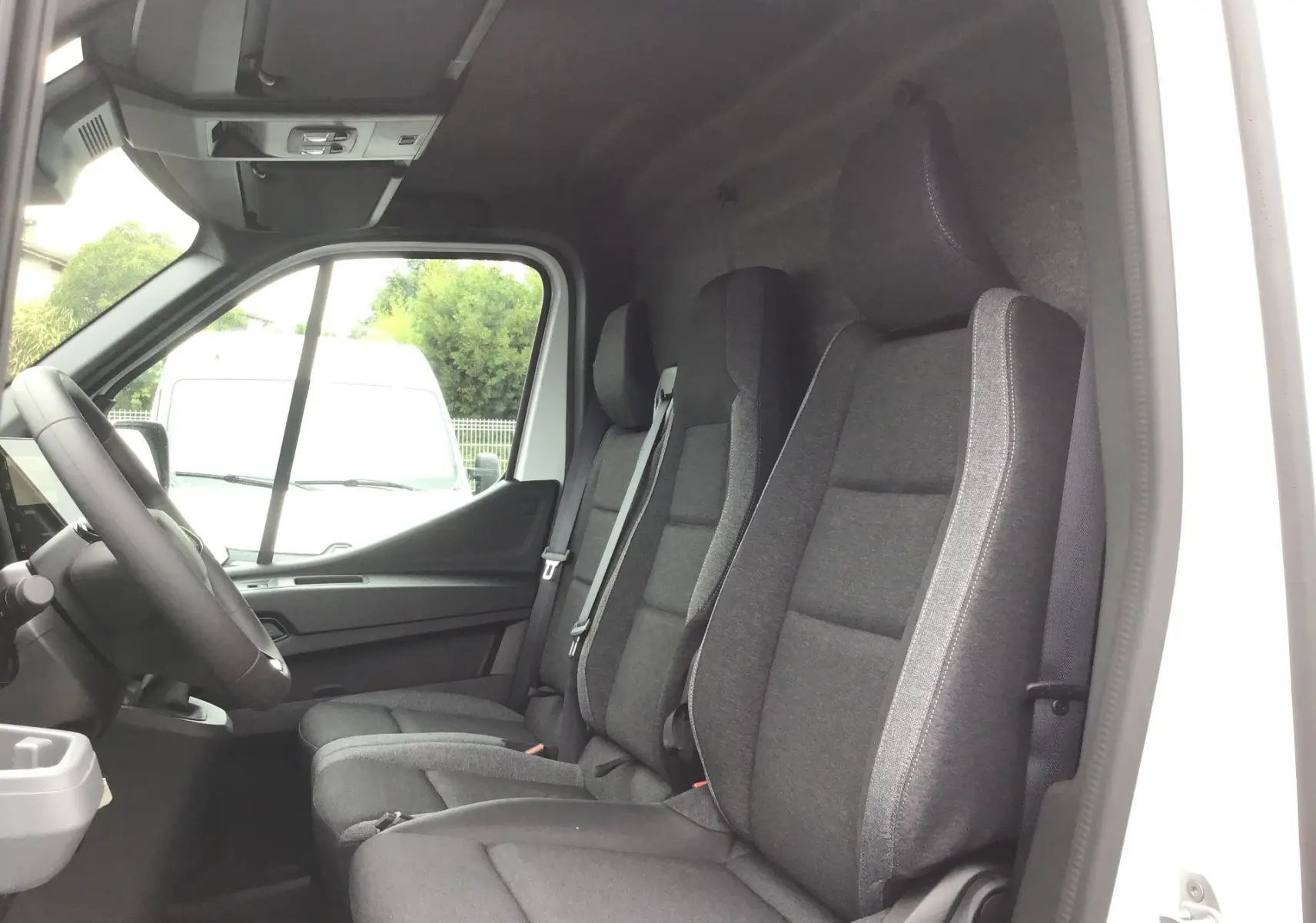 Intérieur du Renault Master blanc 2025 vu côté conducteur, montrant les sièges avant gris et la porte ouverte.