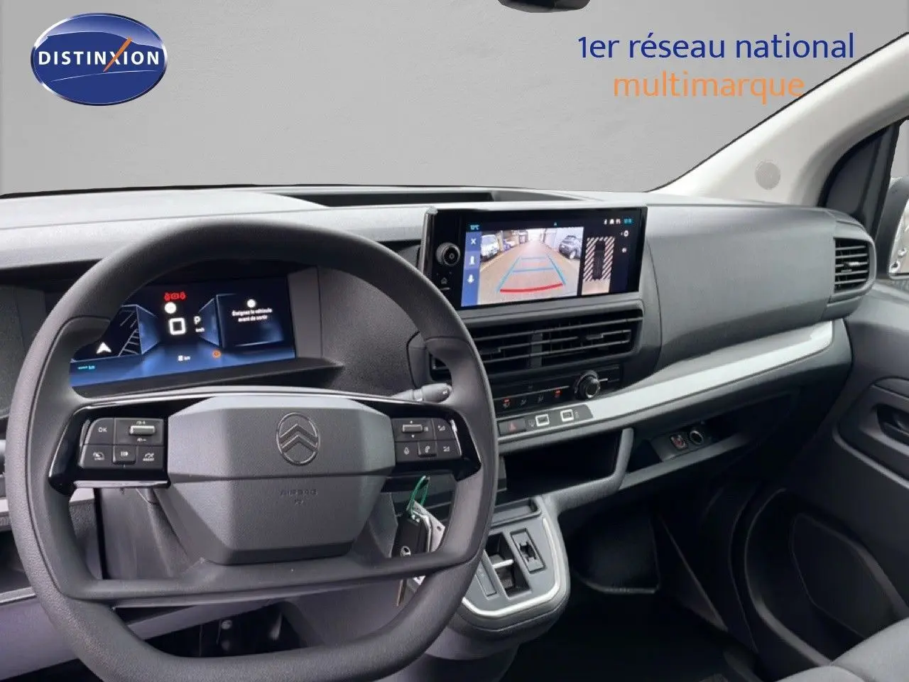 Intérieur du Citroën Jumpy gris, vue du tableau de bord avec volant et écran de caméra de recul visible.