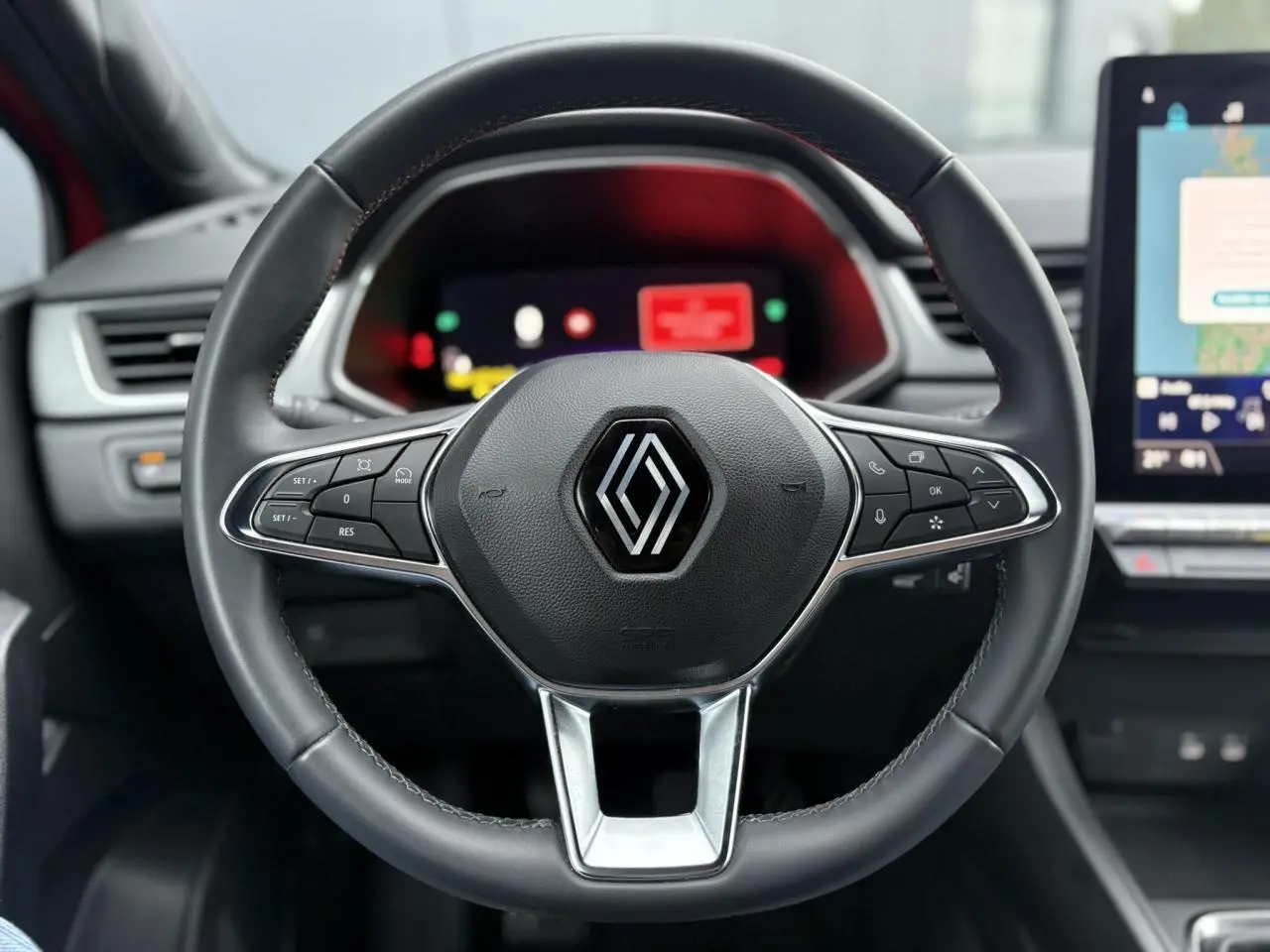 Vue rapprochée du volant noir de la Renault Captur 2025 avec commandes intégrées et tableau de bord numérique flou en arrière-plan.