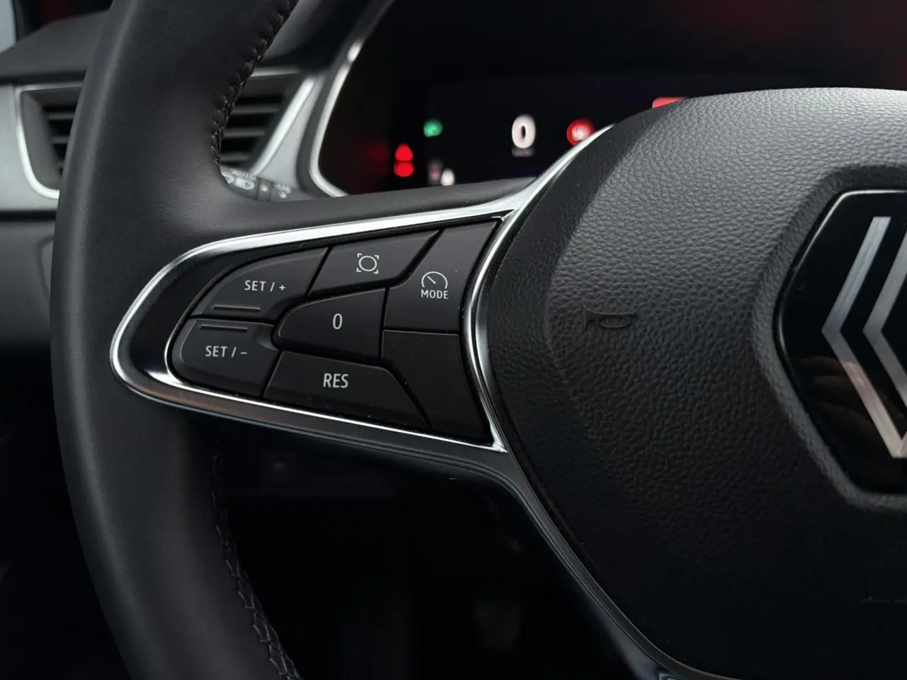 Gros plan sur les commandes à gauche du volant noir du Renault Captur 2025, avec tableau de bord numérique en arrière-plan.