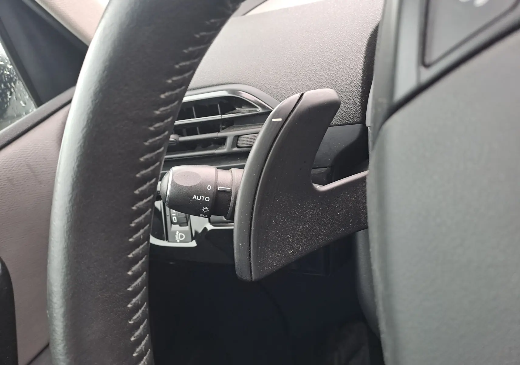 Gros plan sur la palette de changement de vitesse derrière le volant noir d’un Citroën C4 Spacetourer blanc, côté gauche.