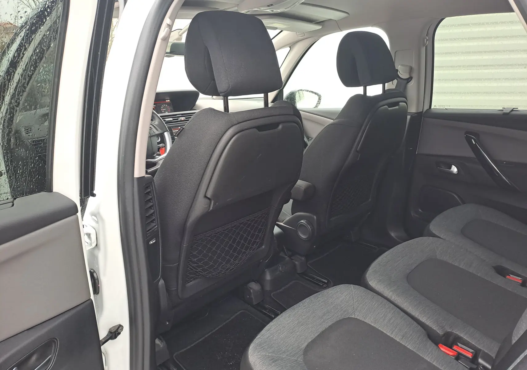 Vue intérieure arrière droite du Citroën C4 Spacetourer blanc 2018, montrant les sièges tissu gris et les dossiers avant avec filets de rangement.