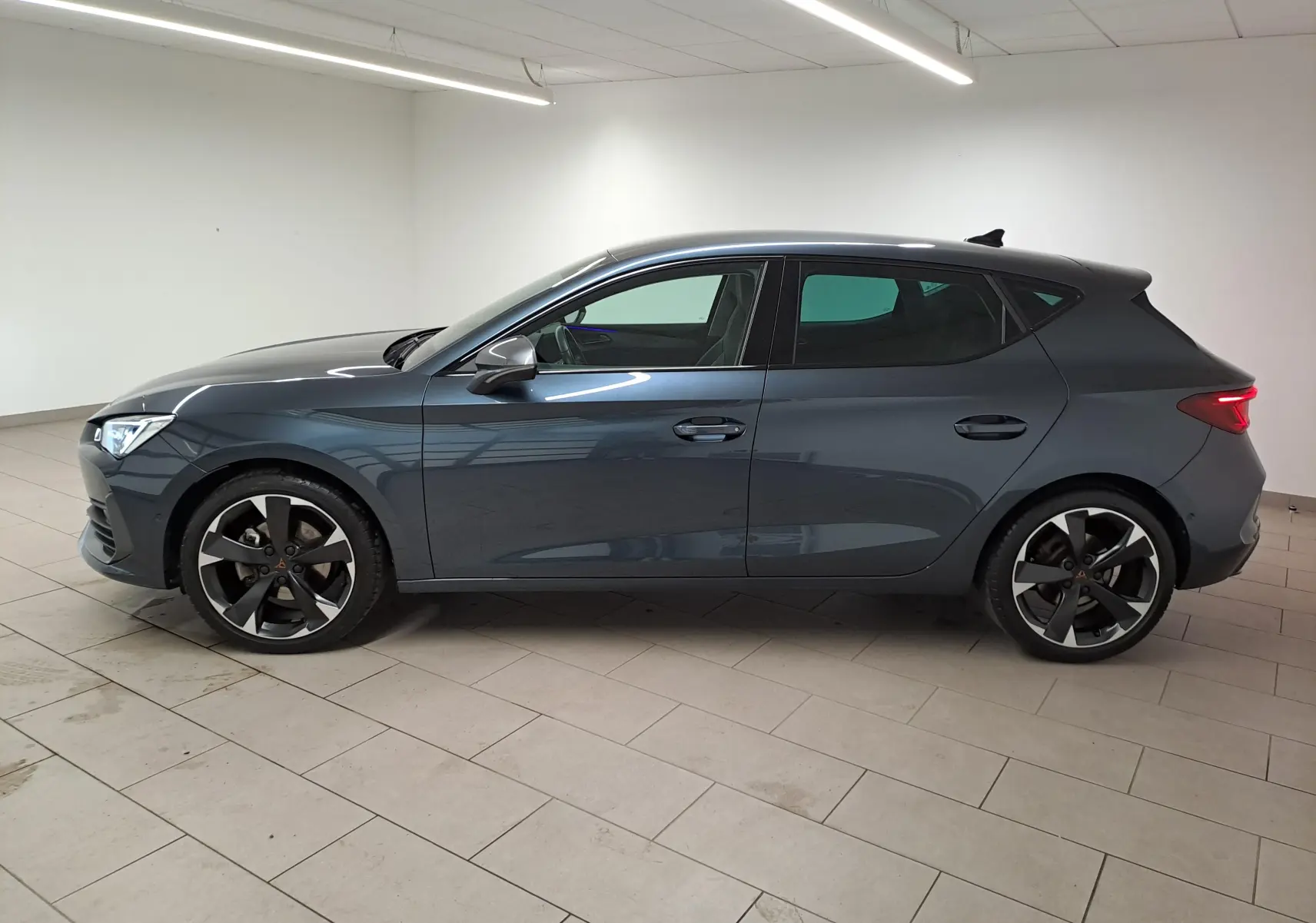 Profil droit d'une CUPRA Leon 1.5 TSI 150 DS7 V gris magnétique 2023, avec jantes noires et design sportif.