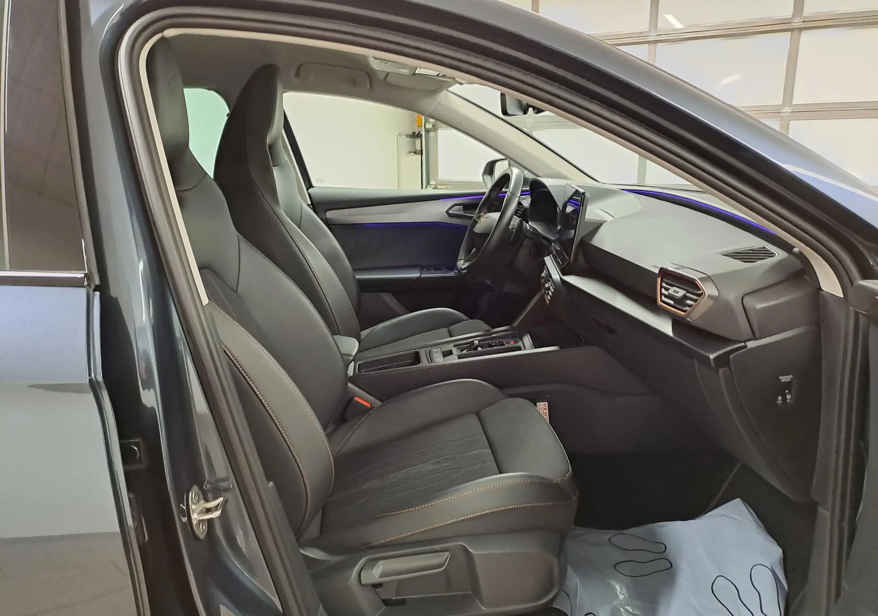 Vue intérieure côté conducteur de la CUPRA Leon 1.5 TSI 150 DS7 gris magnétique, avec sièges sport noirs et tableau de bord moderne.