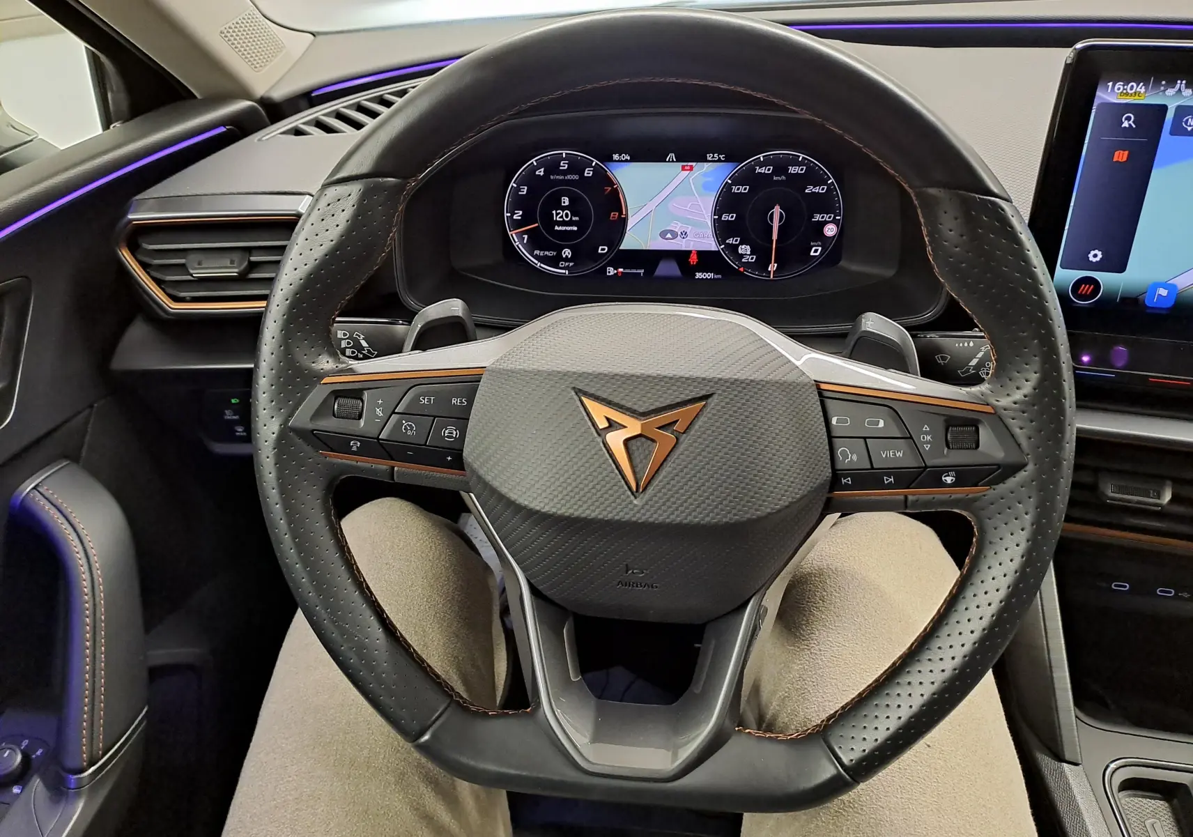 Vue intérieure centrée sur le volant noir perforé avec logo CUPRA cuivre et tableau de bord numérique du Leon 2023.