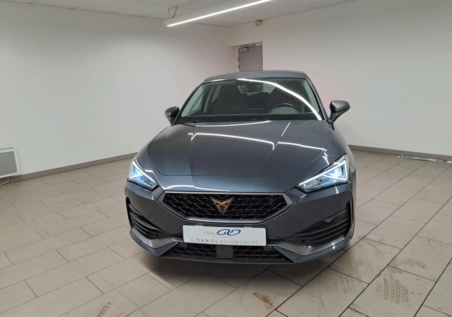 Vue de face d'une CUPRA Leon gris magnétique 2023 avec phares LED allumés et calandre noire distinctive.