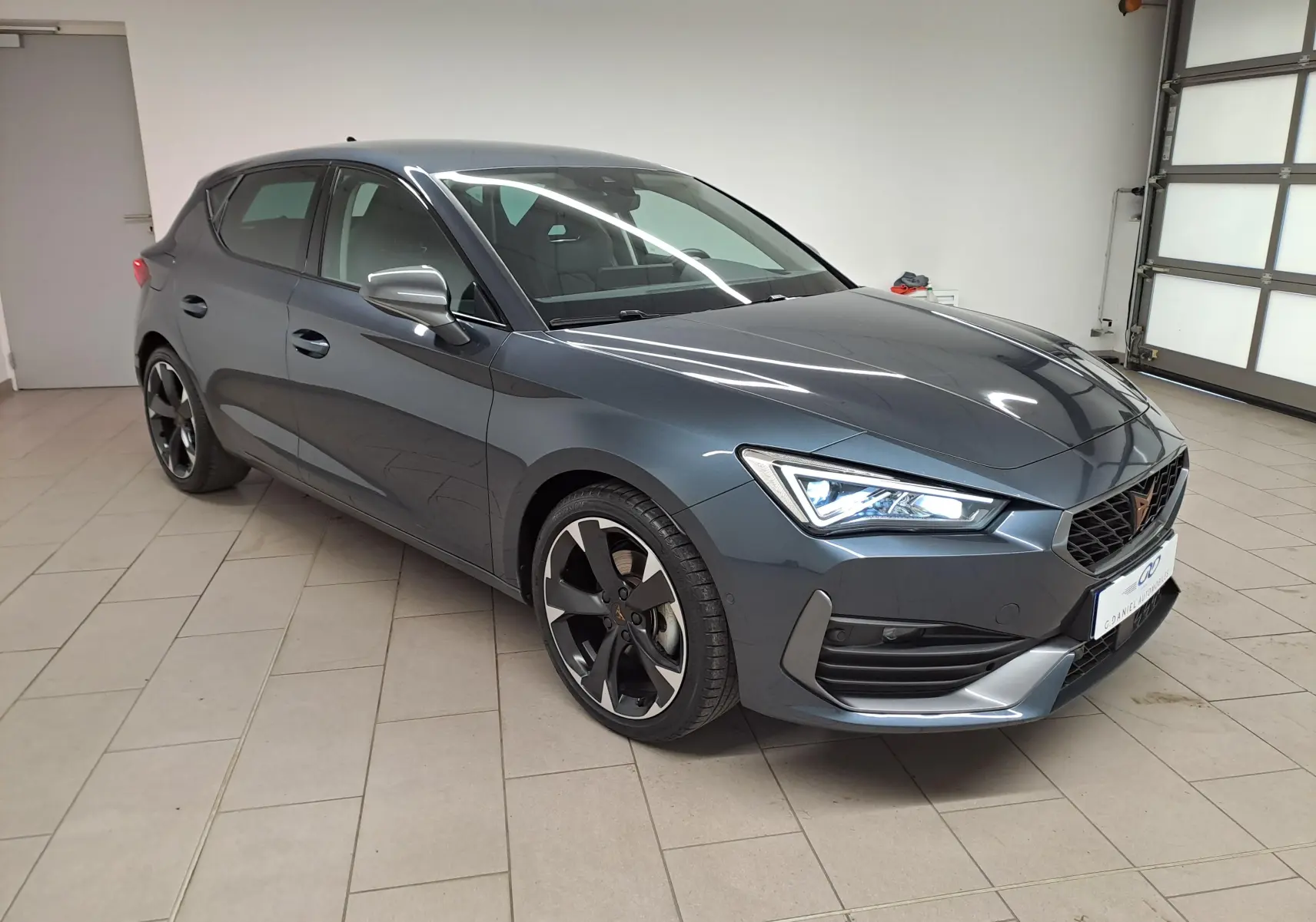 Vue 3/4 avant droite d'une CUPRA Leon 1.5 TSI 150 gris magnétique avec phares LED et jantes noires distinctives.