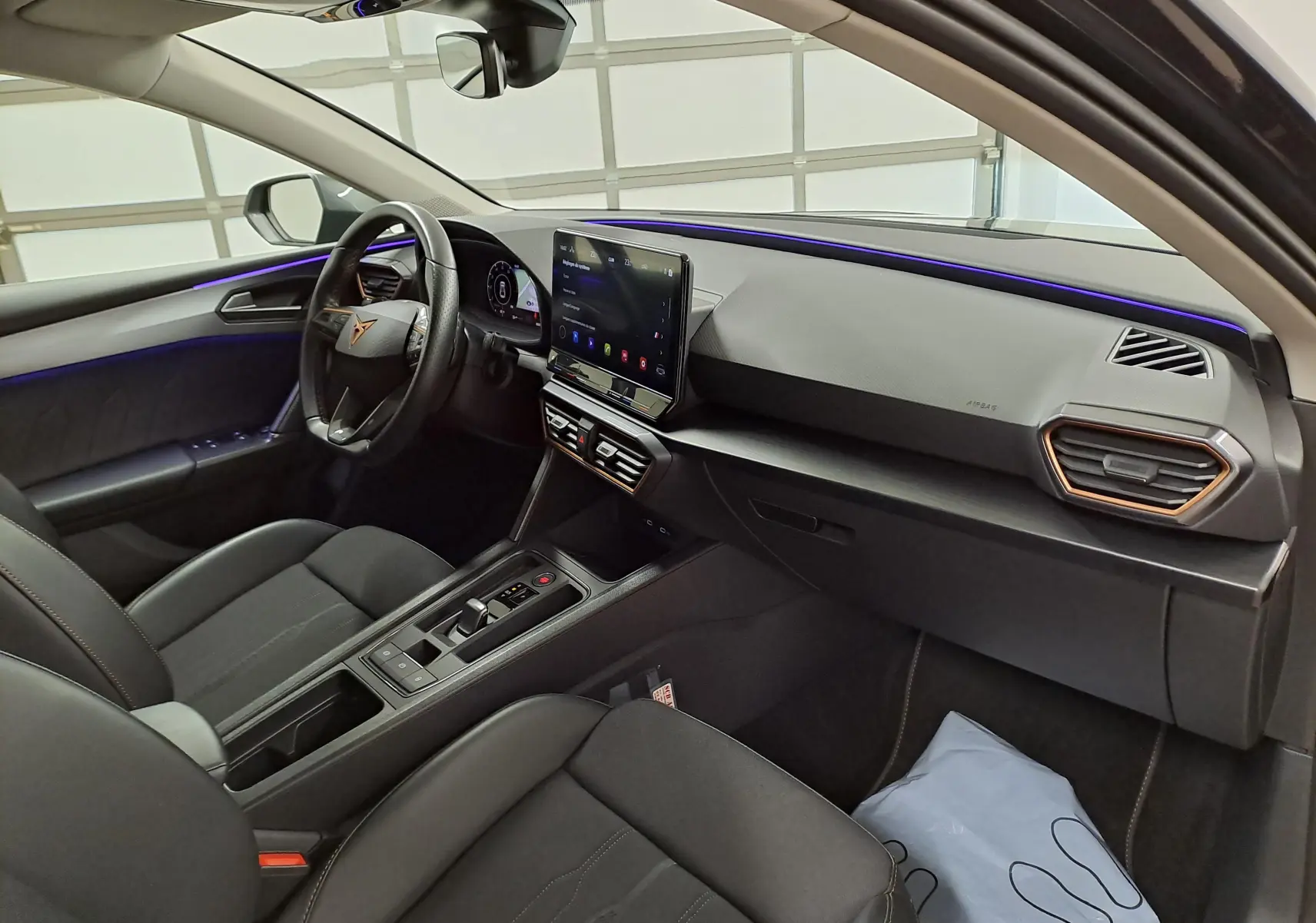 Vue intérieure côté conducteur du CUPRA Leon 1.5 TSI 150 DS7 V 2023, avec tableau de bord moderne et éclairage d’ambiance violet.