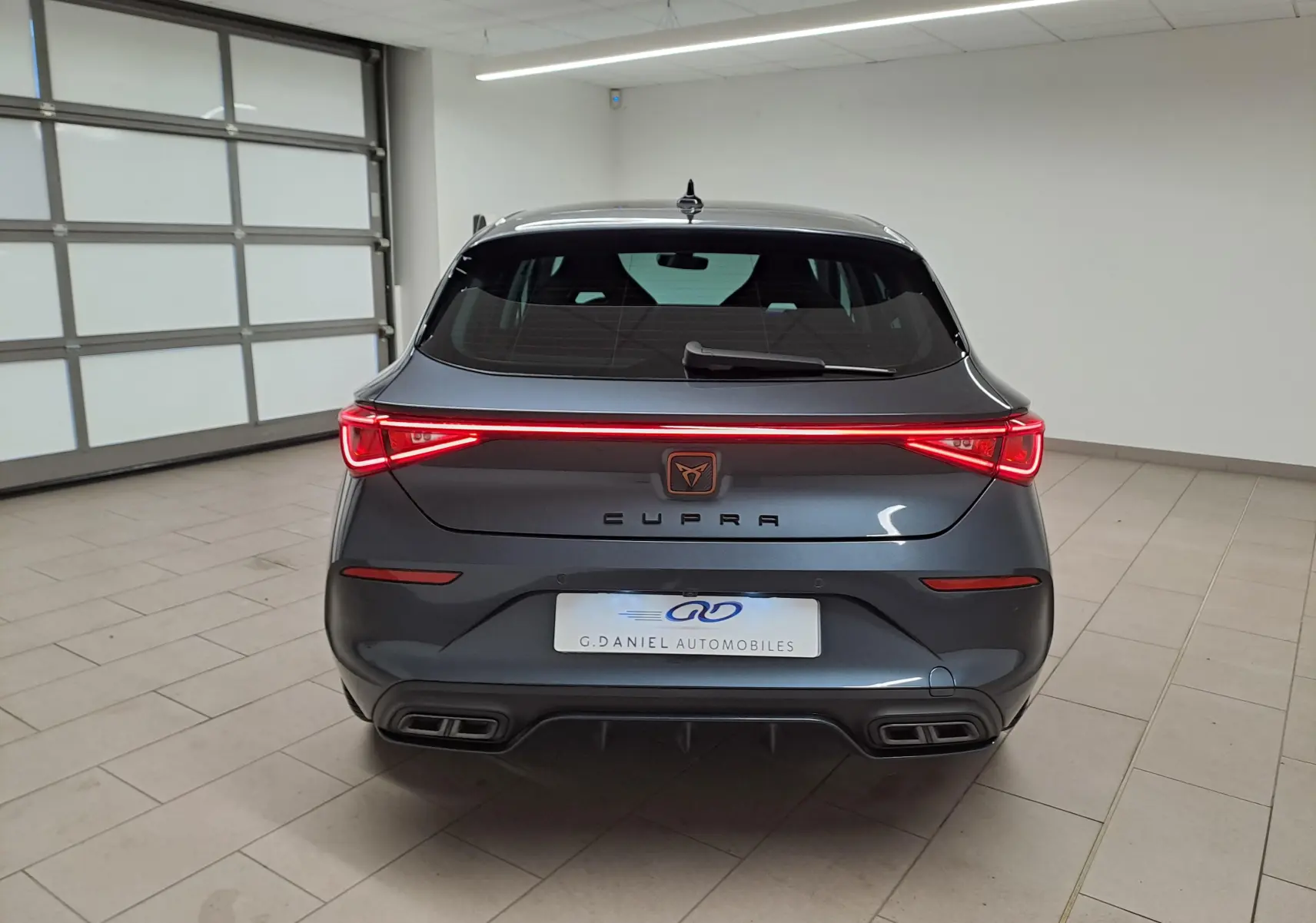 Vue arrière d'une CUPRA Leon gris magnétique avec feux arrière LED en bandeau et double sortie d'échappement rectangulaire.