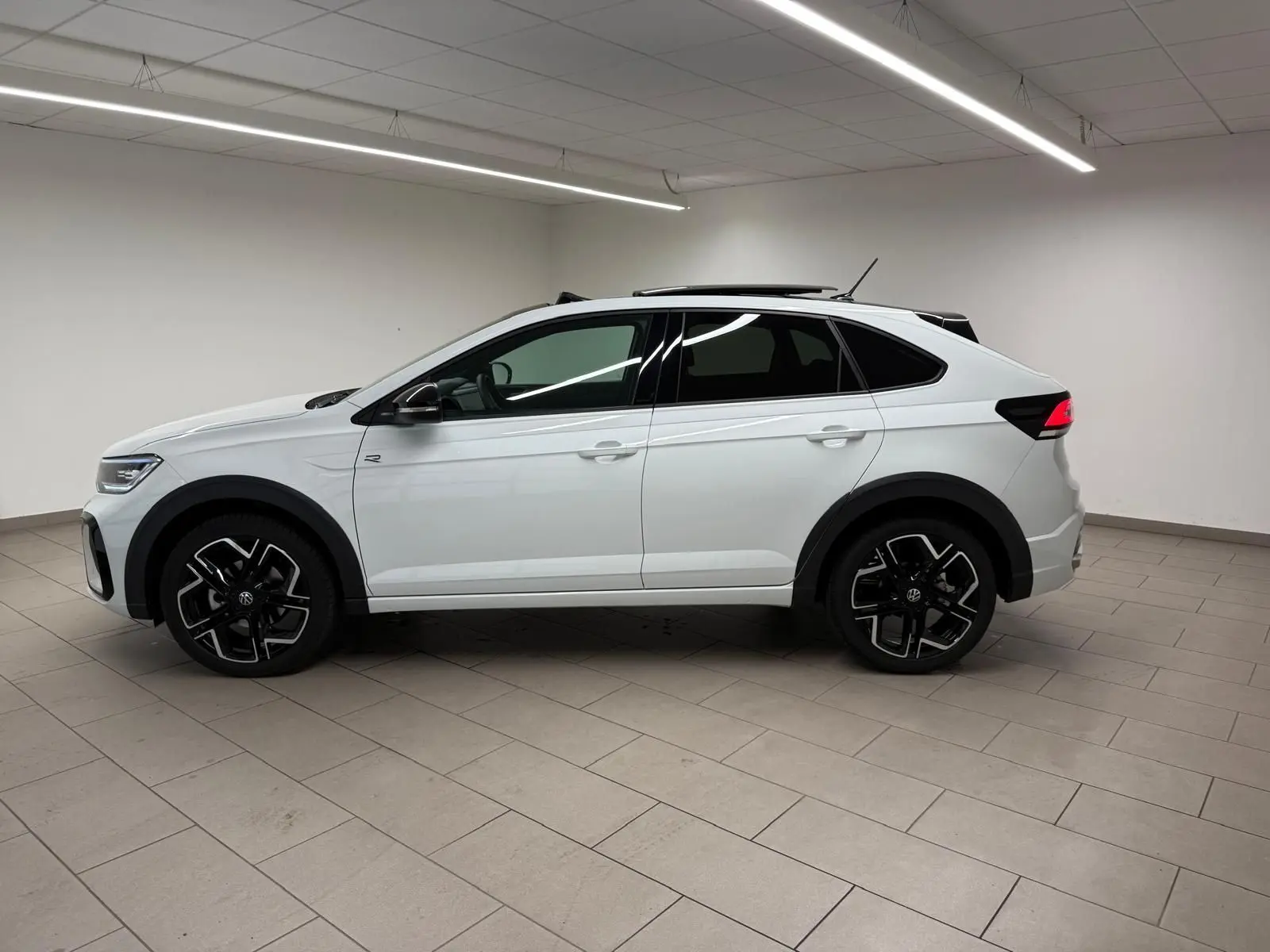 Vue de profil côté gauche d'un Volkswagen Taigo blanc pur avec toit noir et jantes alliage noires en intérieur neutre.