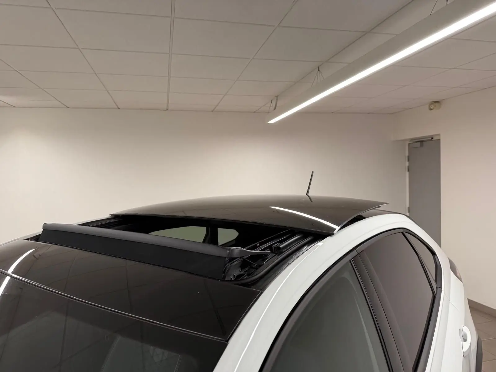 Vue 3/4 arrière droite d'un Volkswagen Taigo blanc pur avec toit ouvrant électrique noir partiellement ouvert.