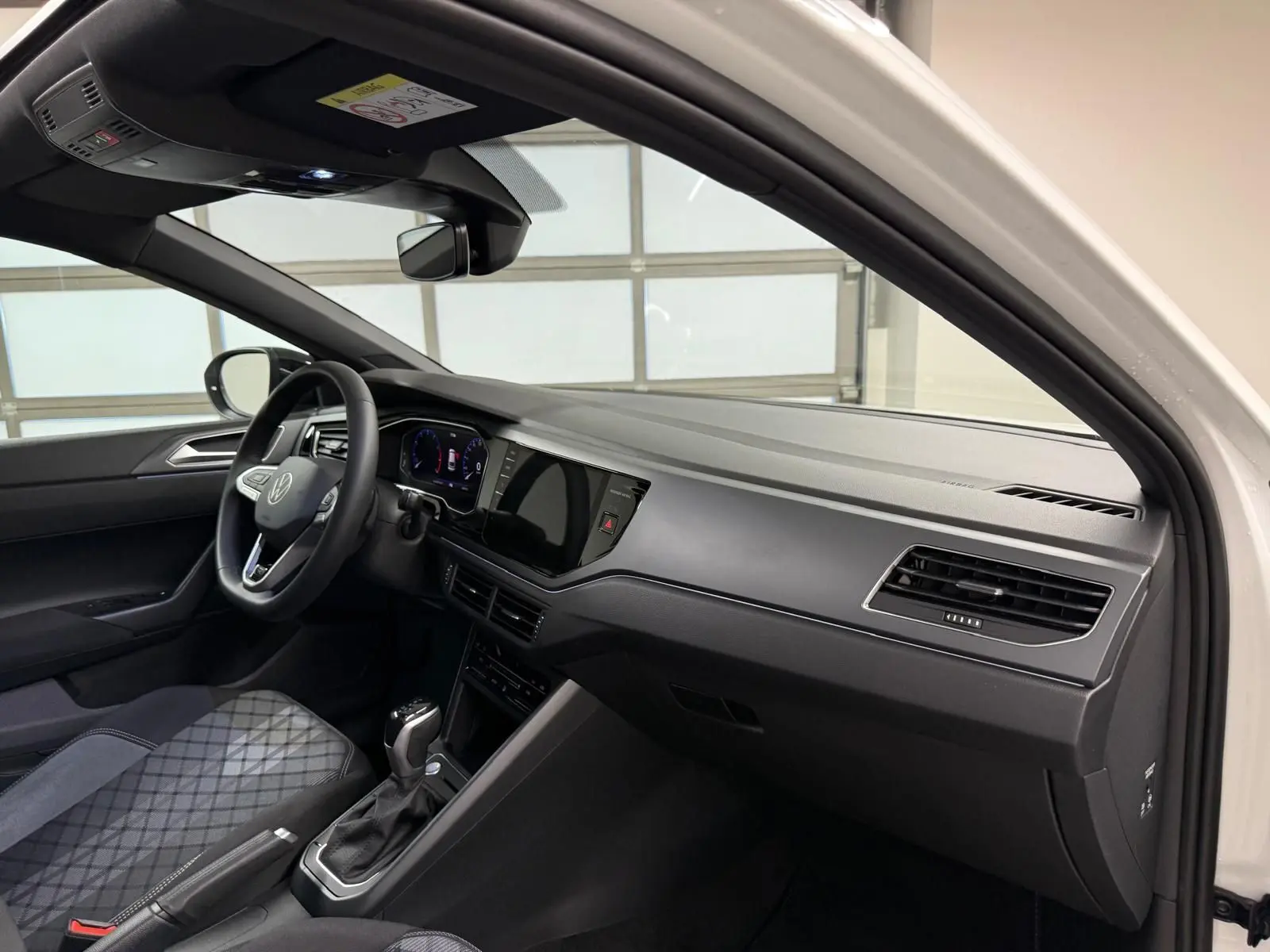 Vue intérieure côté conducteur du Volkswagen Taigo blanc pur, tableau de bord noir avec écran tactile et volant cuir multifonctions.