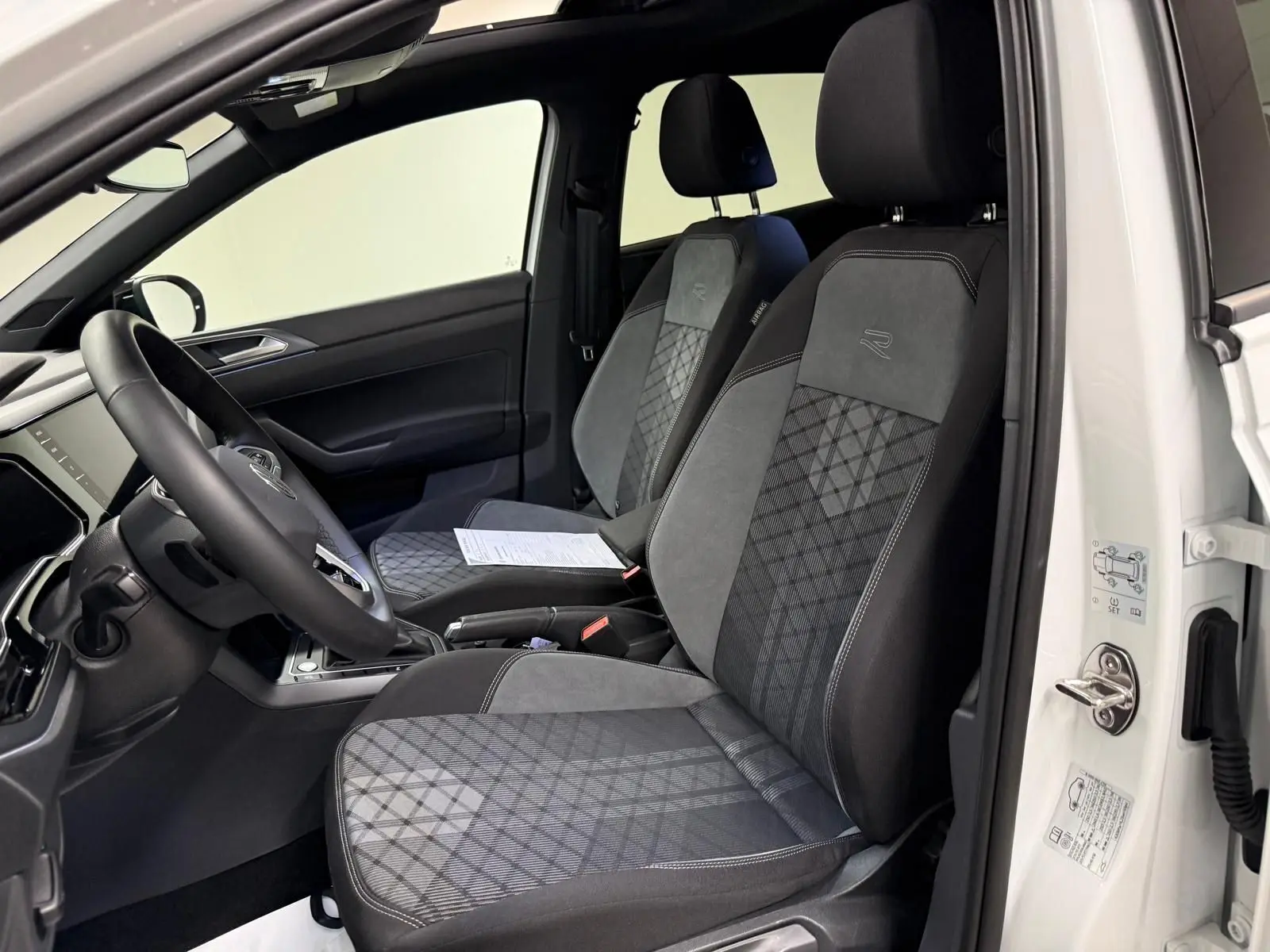 Vue intérieure côté conducteur du Volkswagen Taigo blanc, sièges sport en tissu noir et gris avec logo R-Line brodé.