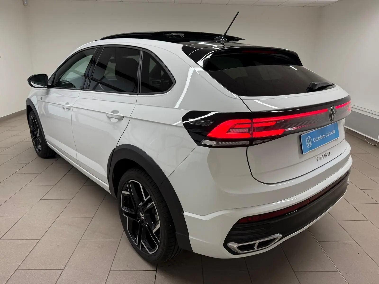 Vue 3/4 arrière droite du Volkswagen Taigo blanc pur avec toit noir et feux arrière LED allumés en intérieur.