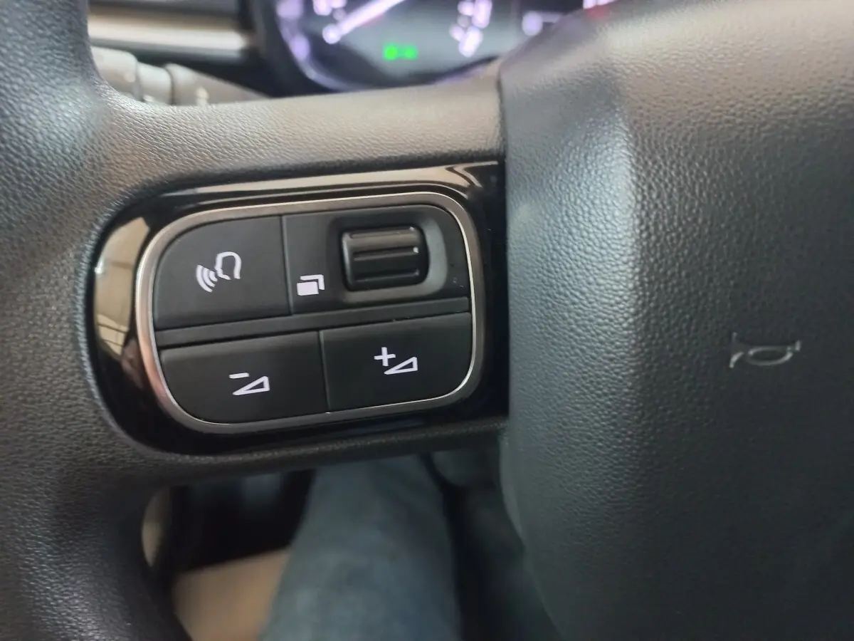 Gros plan sur les commandes multifonctions à gauche du volant noir du Citroën C3 BlueHDi 2024.