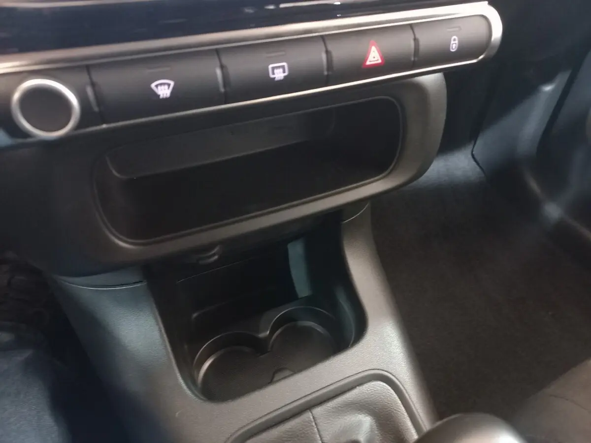 Gros plan sur la console centrale noire de la Citroën C3 2024, avec porte-gobelets et boutons de commande alignés.